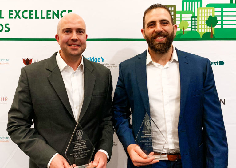 Two men smile to camera while holding awards